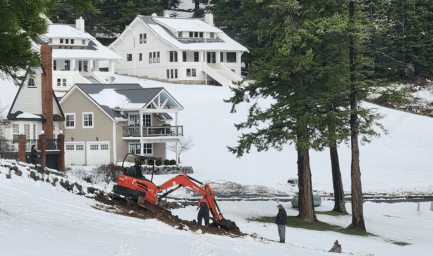 An excavator working on a large hill in the snow.